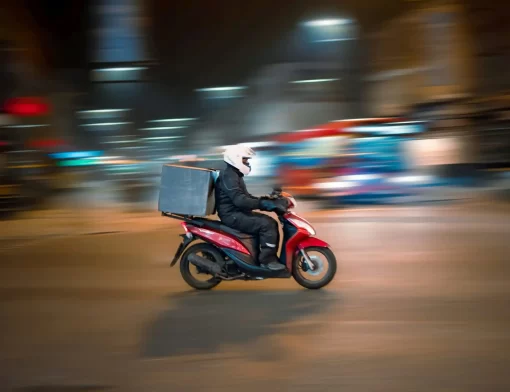 Motoboy pilotando uma das motos para entrega à noite em via urbana