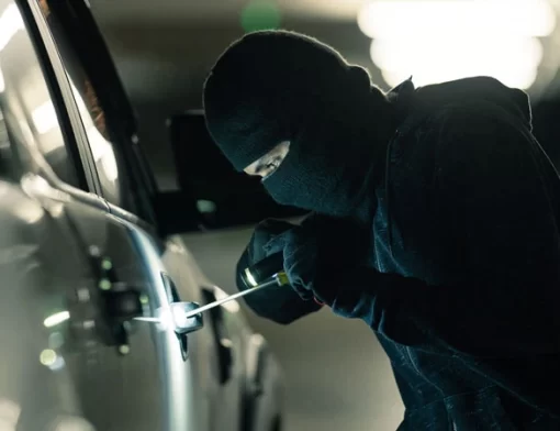 Homem tentando arrombar a porta de um carro com chave de fenda, representando um sinistro de veículo por furto
