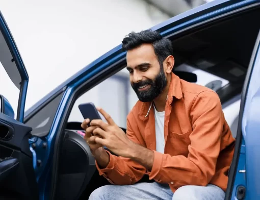 Homem sentado no carro usando celular para contratar seguro por assinatura de forma digital e prática