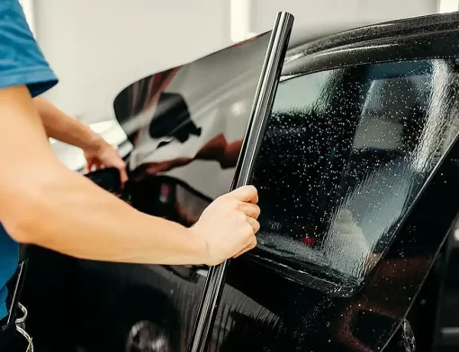Instalador aplica insulfilm automotivo no vidro lateral do carro, alinhando a película para conforto térmico e menos ofuscamento.